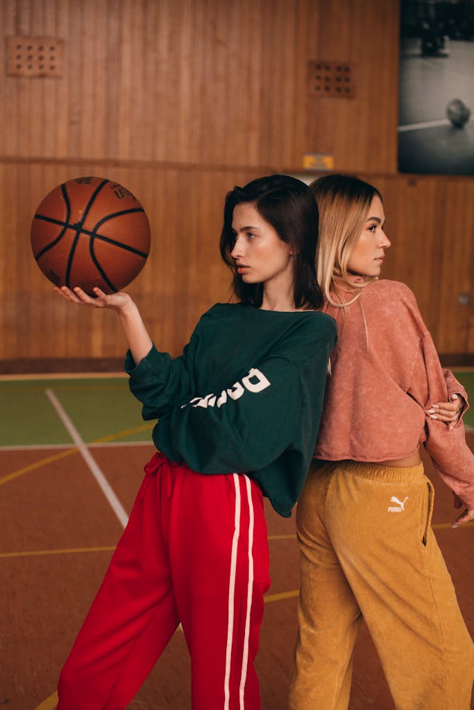 Two women posing with a basketball on an indoor court in vibrant sportswear.