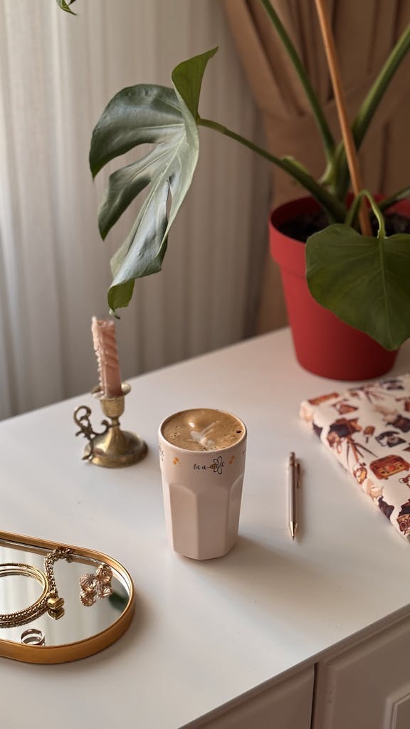 Warm and cozy desk setup with coffee, monstera plant, and accessories.