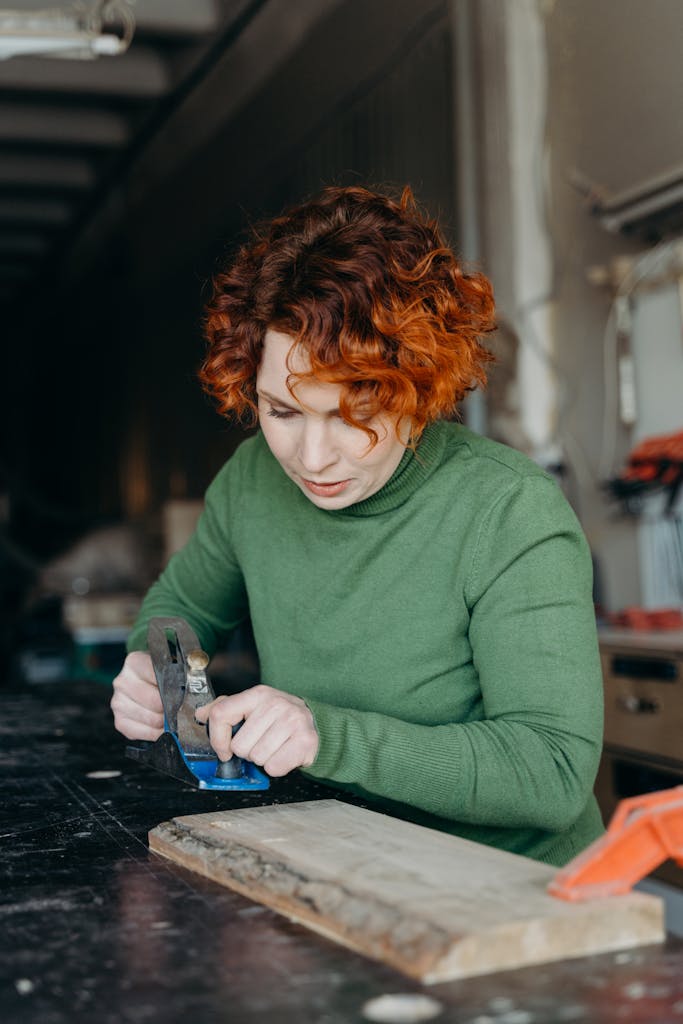 Woman craftswoman focused on woodworking in a workshop setting. Indoors, warm lighting.