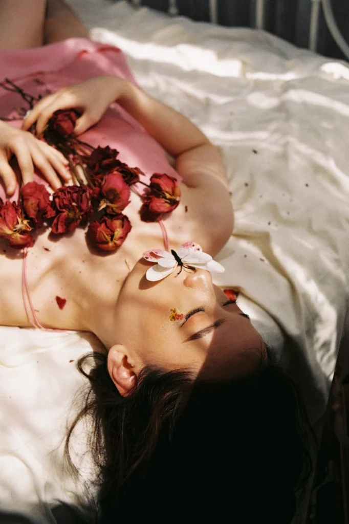 A woman lies peacefully with a butterfly on red roses, evoking serenity.