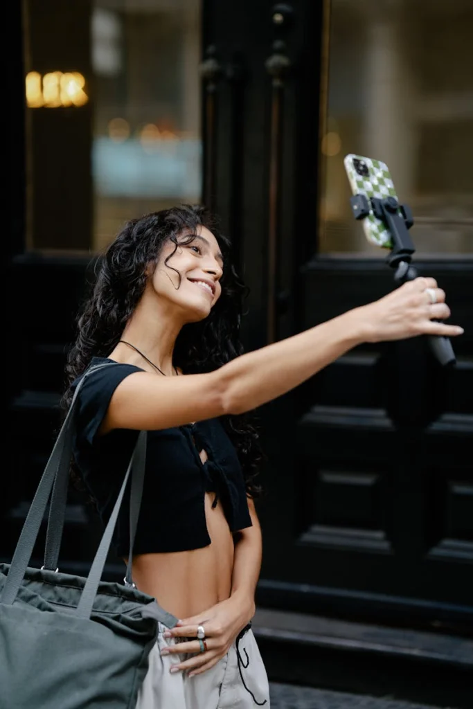 Smiling woman capturing a selfie with a smartphone on a stick in an urban environment.