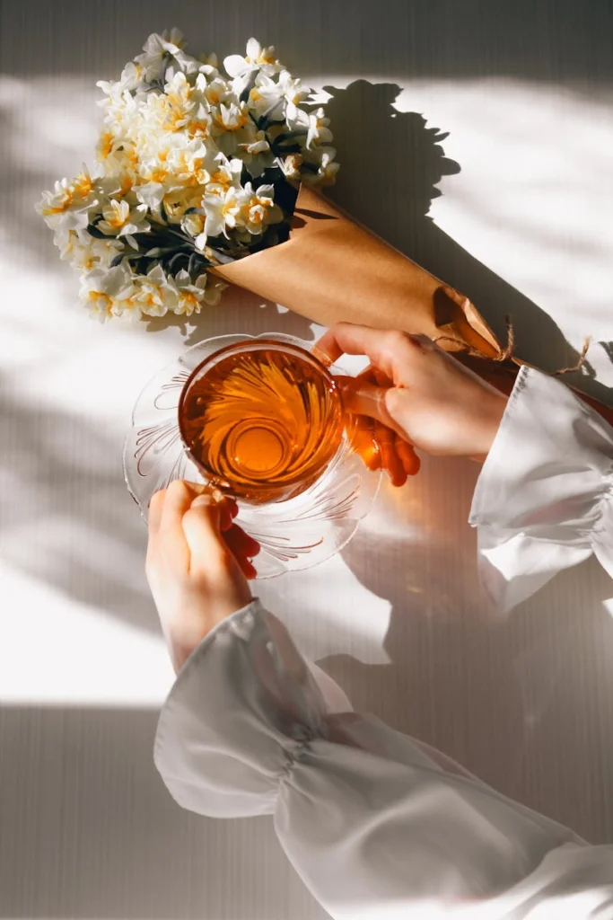 Dainty hands hold tea beside a delicate bouquet under warm sunlight, creating a romantic, serene ambiance.