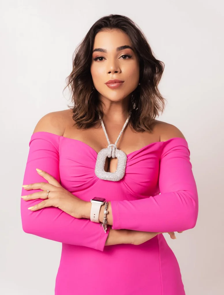 A young woman exuding confidence in a stylish pink off-shoulder dress against a plain background.