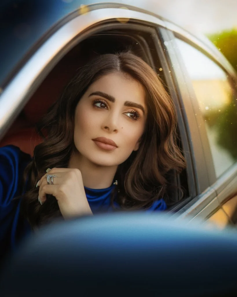Portrait of a woman with curly hair looking contemplatively out of a car window, wearing elegant attire.