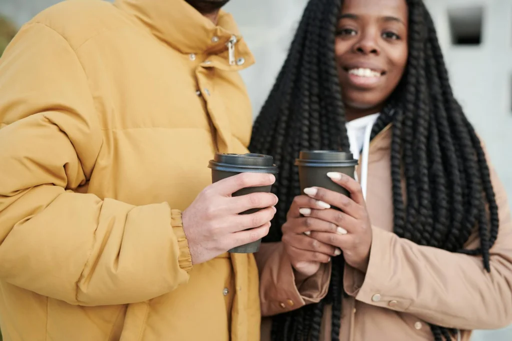 Smiling couple with takeaway coffee cups, dressed in warm winter jackets, sharing a moment outdoors.