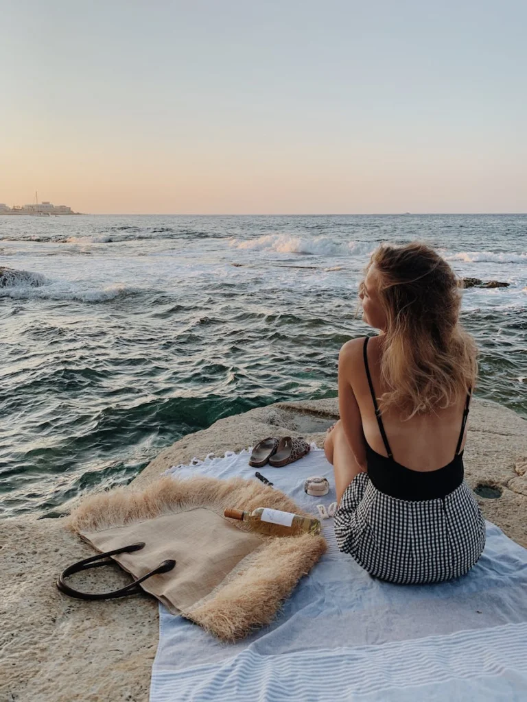 Woman enjoys peaceful ocean view at sunset on a rocky beach.