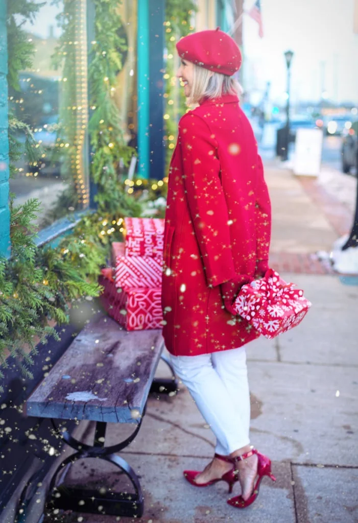 Woman in red coat carrying Christmas presents on a snowy city street.