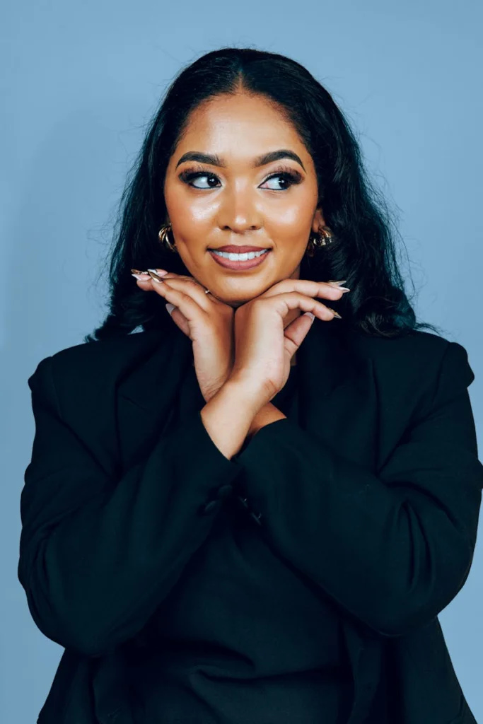 Glamorous woman with long dark hair posing in a black blazer against a blue background.