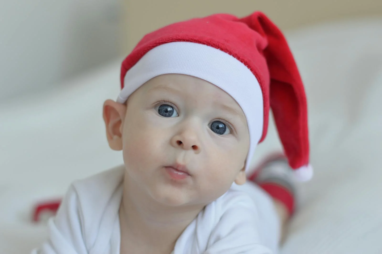 A cute baby with blue eyes wearing a red Santa hat, capturing the festive Christmas spirit indoors.