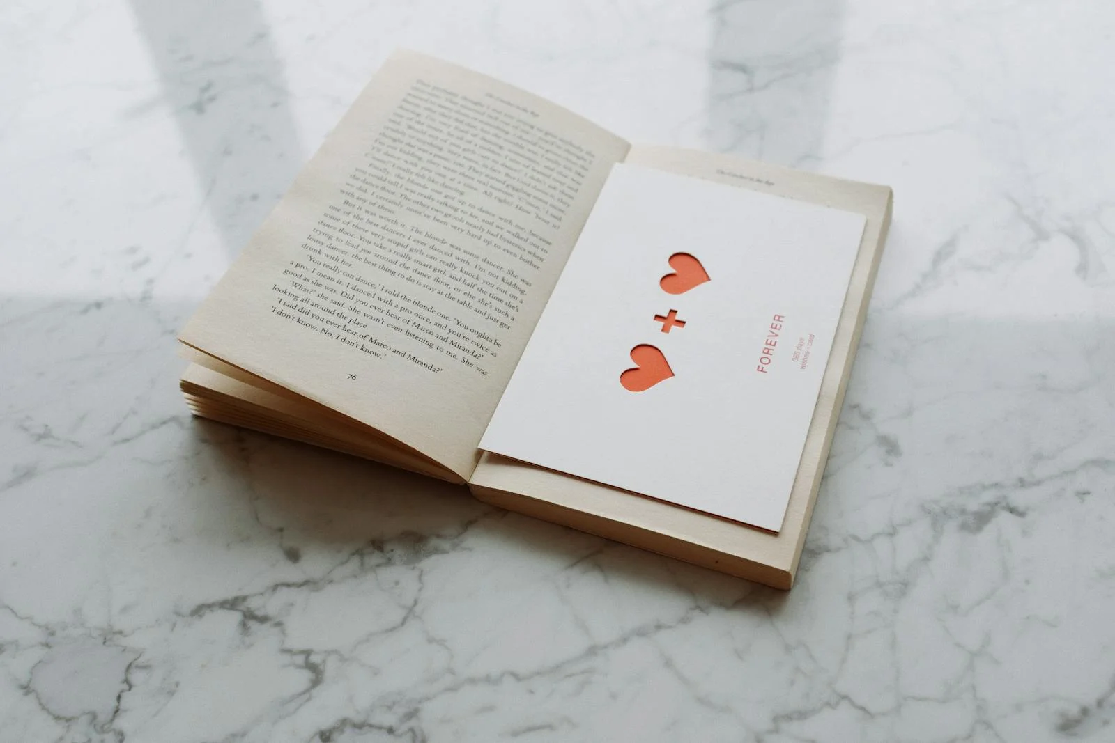 An open book with a love-themed card featuring cut-out hearts on a marble surface.