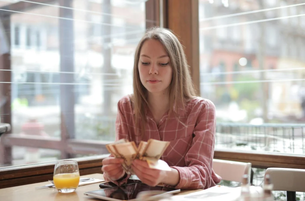 Young woman counting money in a cafe, showcasing modern lifestyle and leisure.