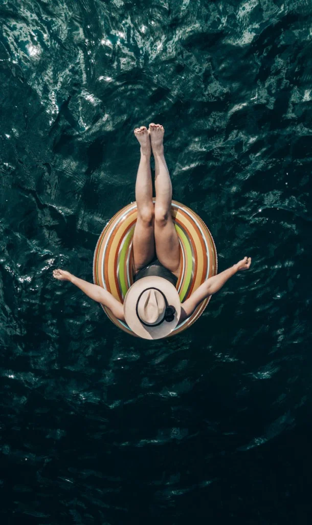 Top view of unrecognizable barefoot tourist in hat lying in inflatable ring on rippled sea during summer trip
