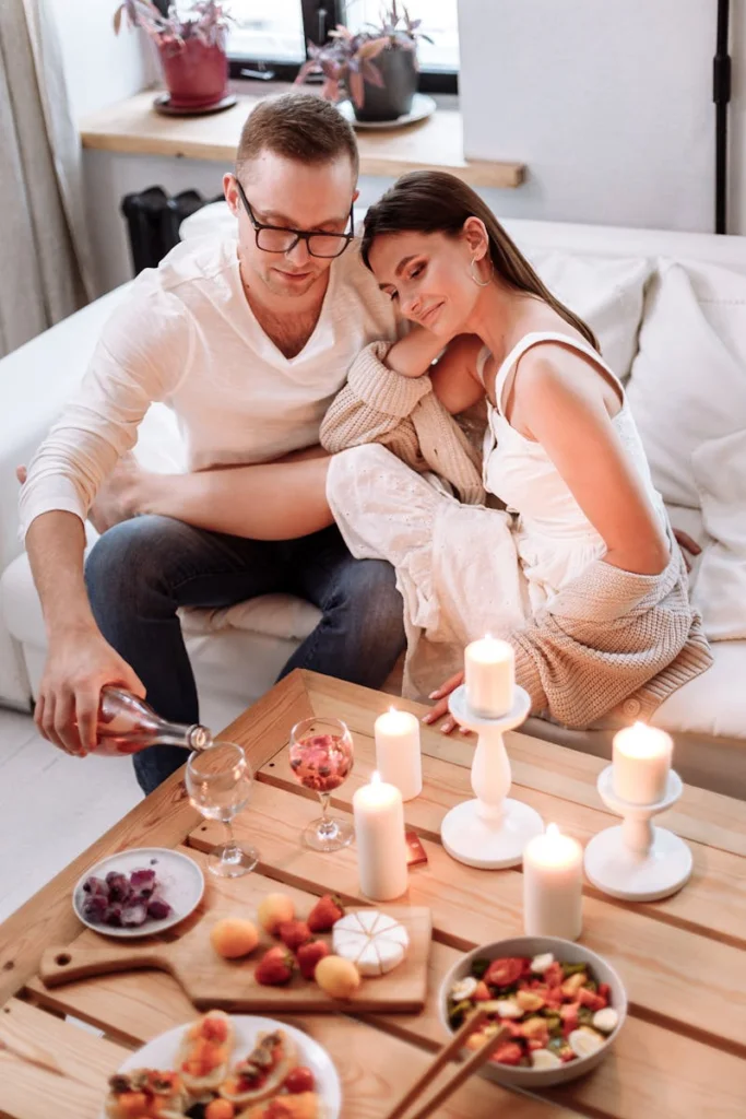 A couple enjoying a cozy romantic dinner with candles, wine, and fruit indoors.