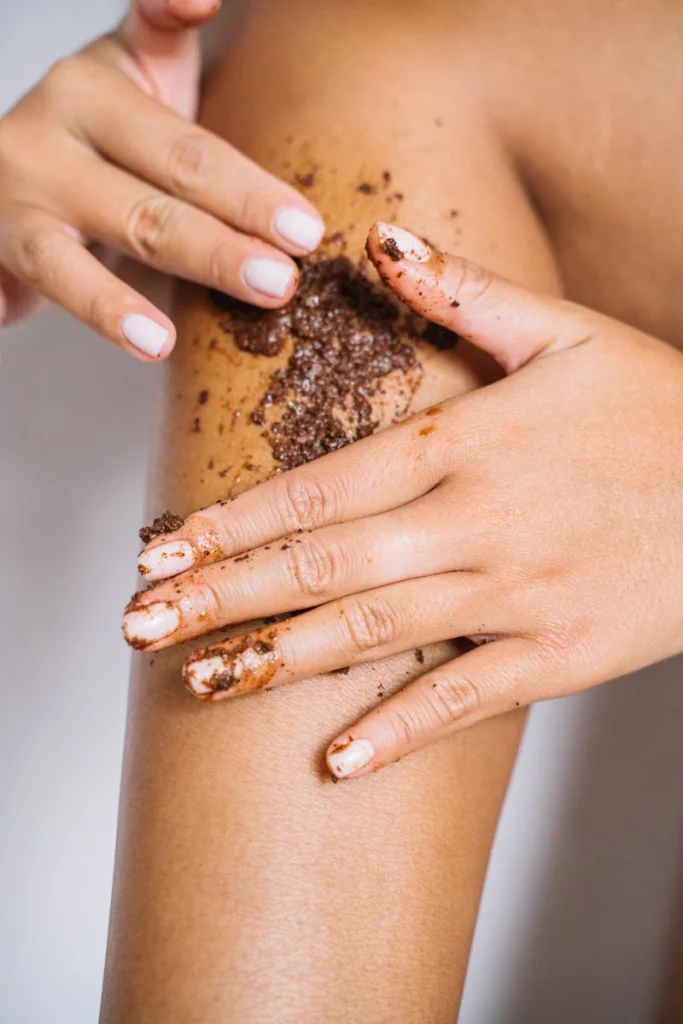 Close-up shot of hands applying coffee scrub to a leg for skin care.