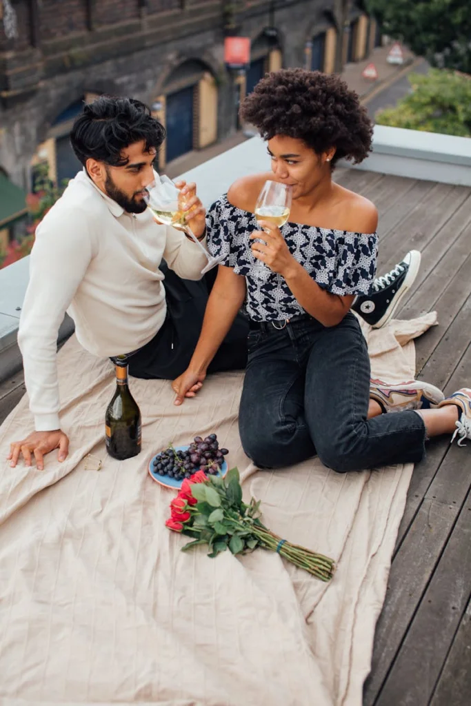Couple enjoying a romantic rooftop picnic with wine, grapes, and roses.