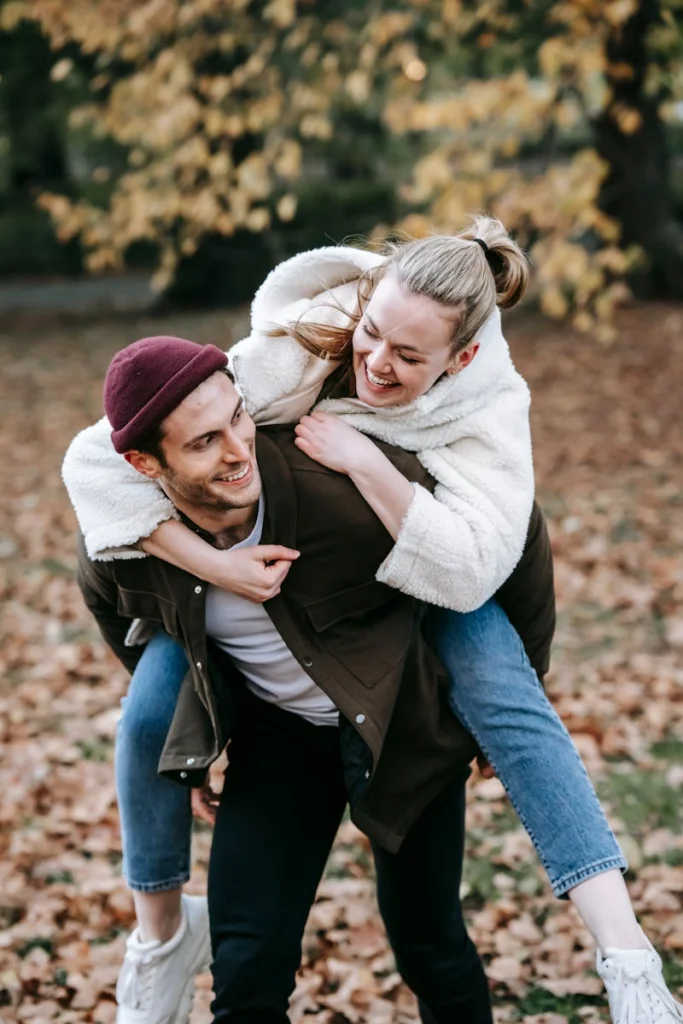Happy young couple in warm clothes laughing and enjoying weekend on blurred background of autumn trees