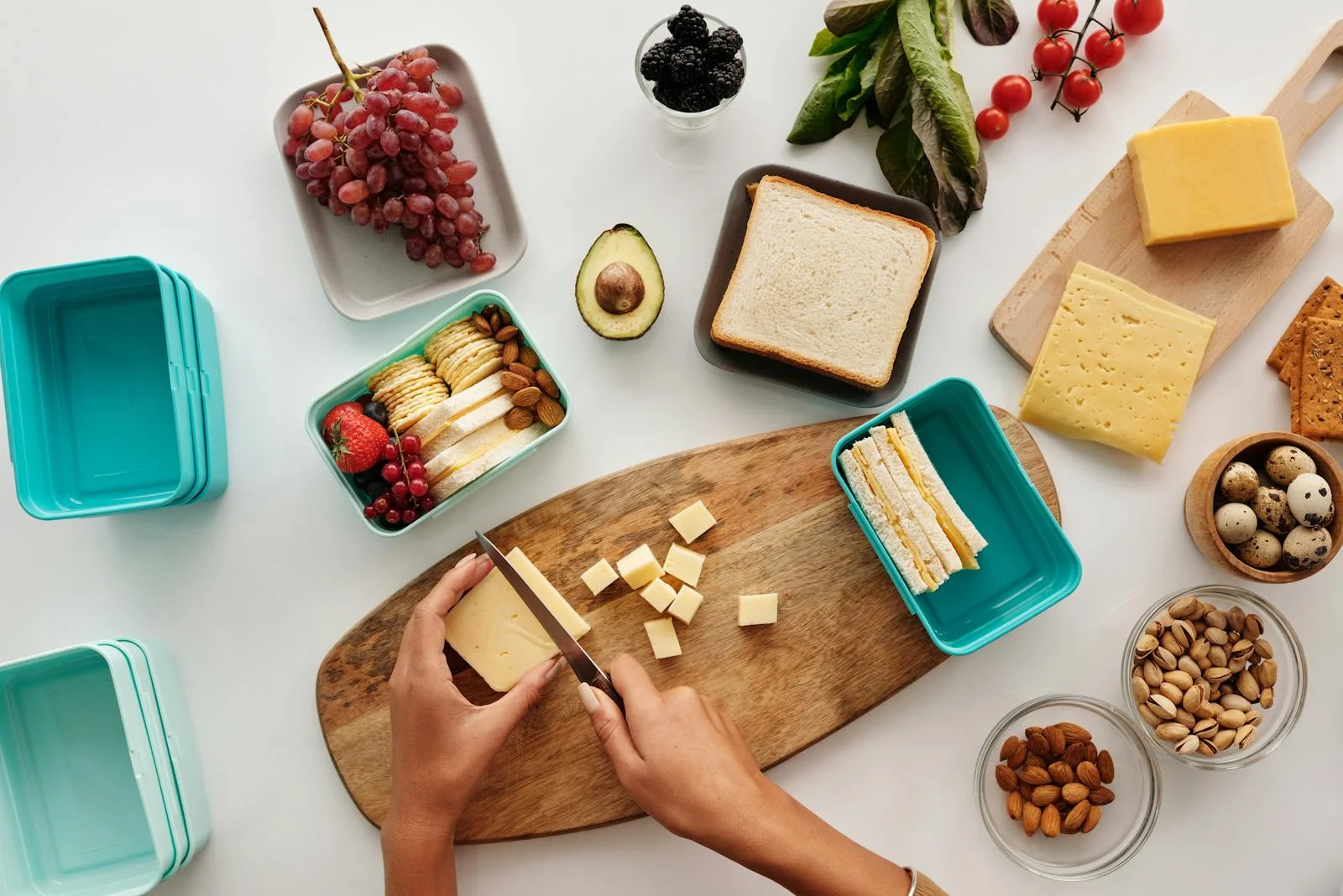 Top view of a person preparing a cheese and fruit spread with various ingredients on wooden board.