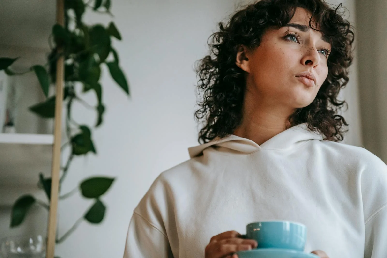 Thoughtful woman holding coffee cup, visually pondering indoors.