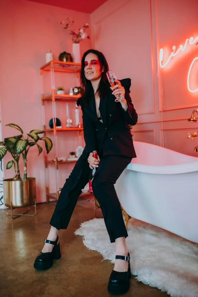 Stylish woman in black suit enjoying a celebration with a drink, vibrant indoor setting.