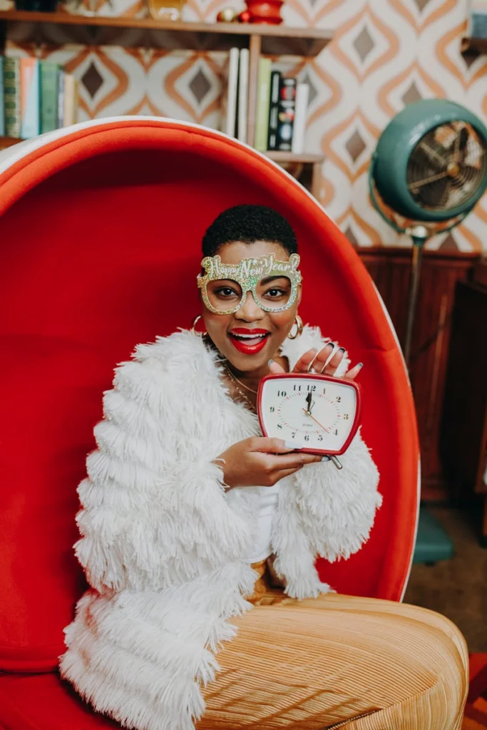 Cheerful woman celebrating New Year's Eve with a clock, wearing festively themed glasses.