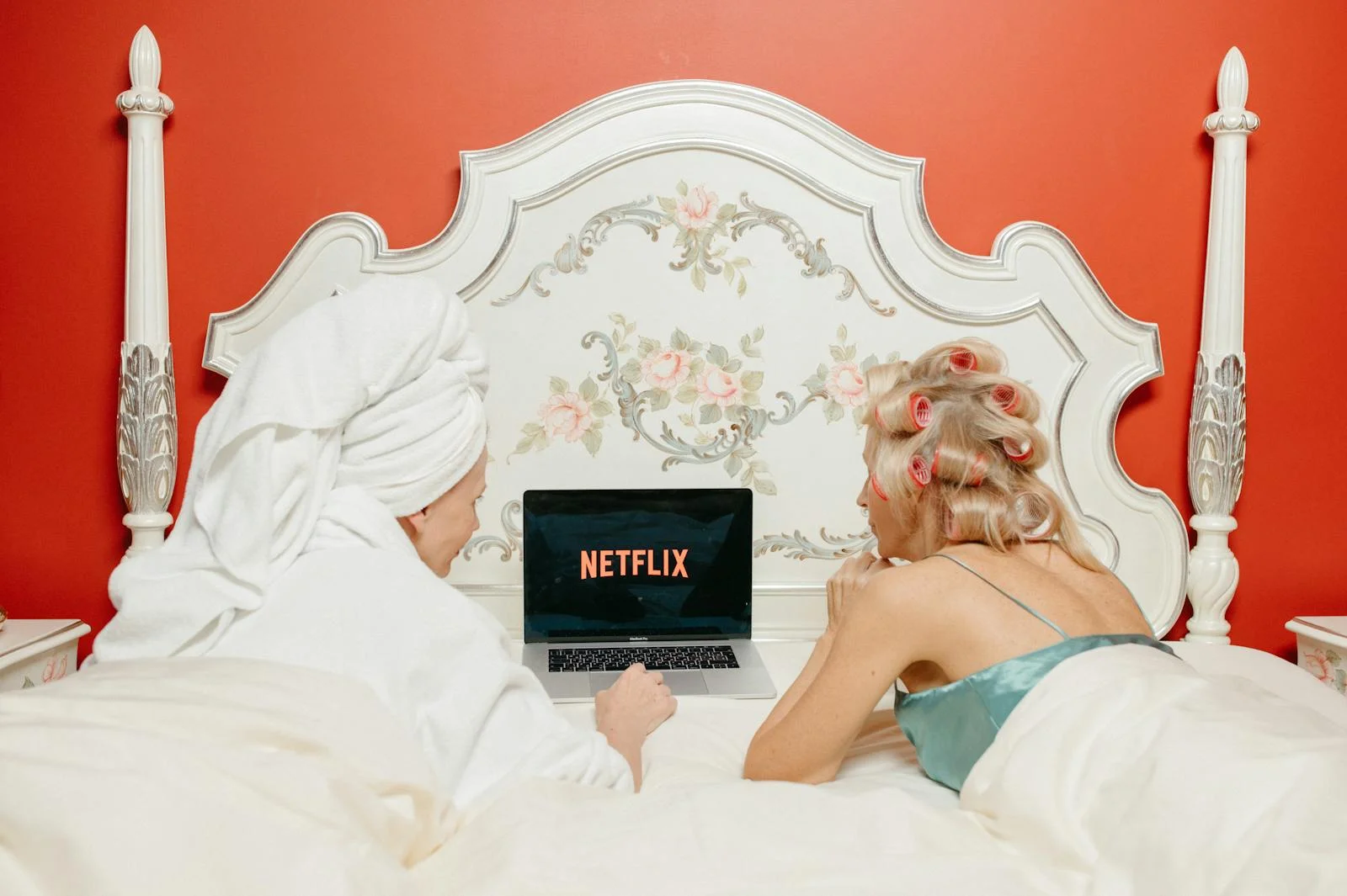 Two women enjoying Netflix in a cozy, vintage-style bedroom with red walls.
