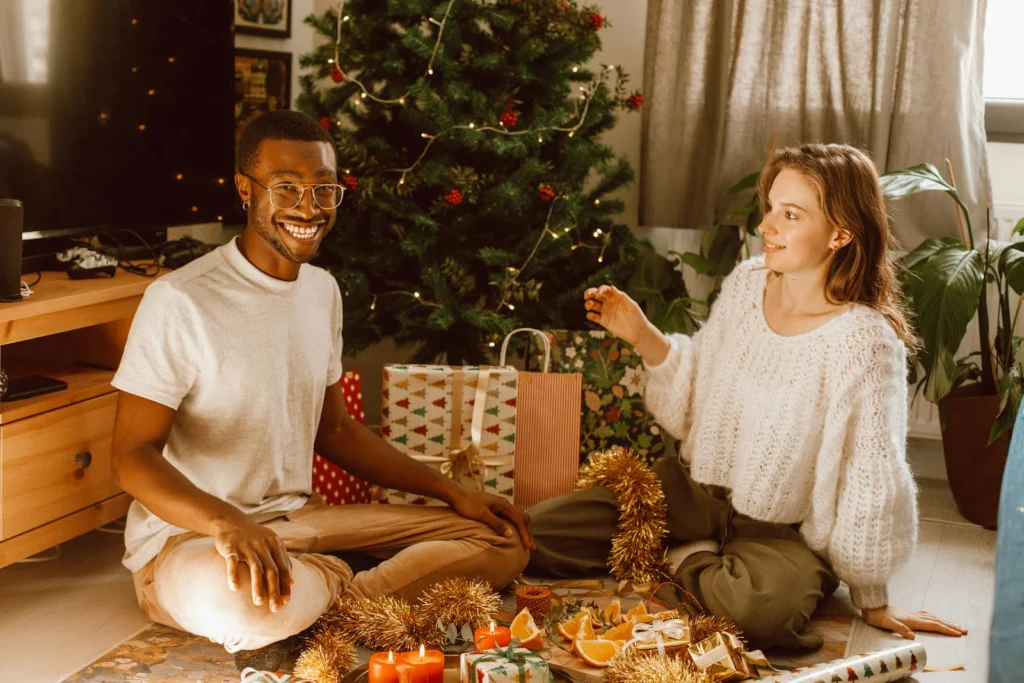 Smiling couple enjoying Christmas decorations and gifts by the tree indoors.
