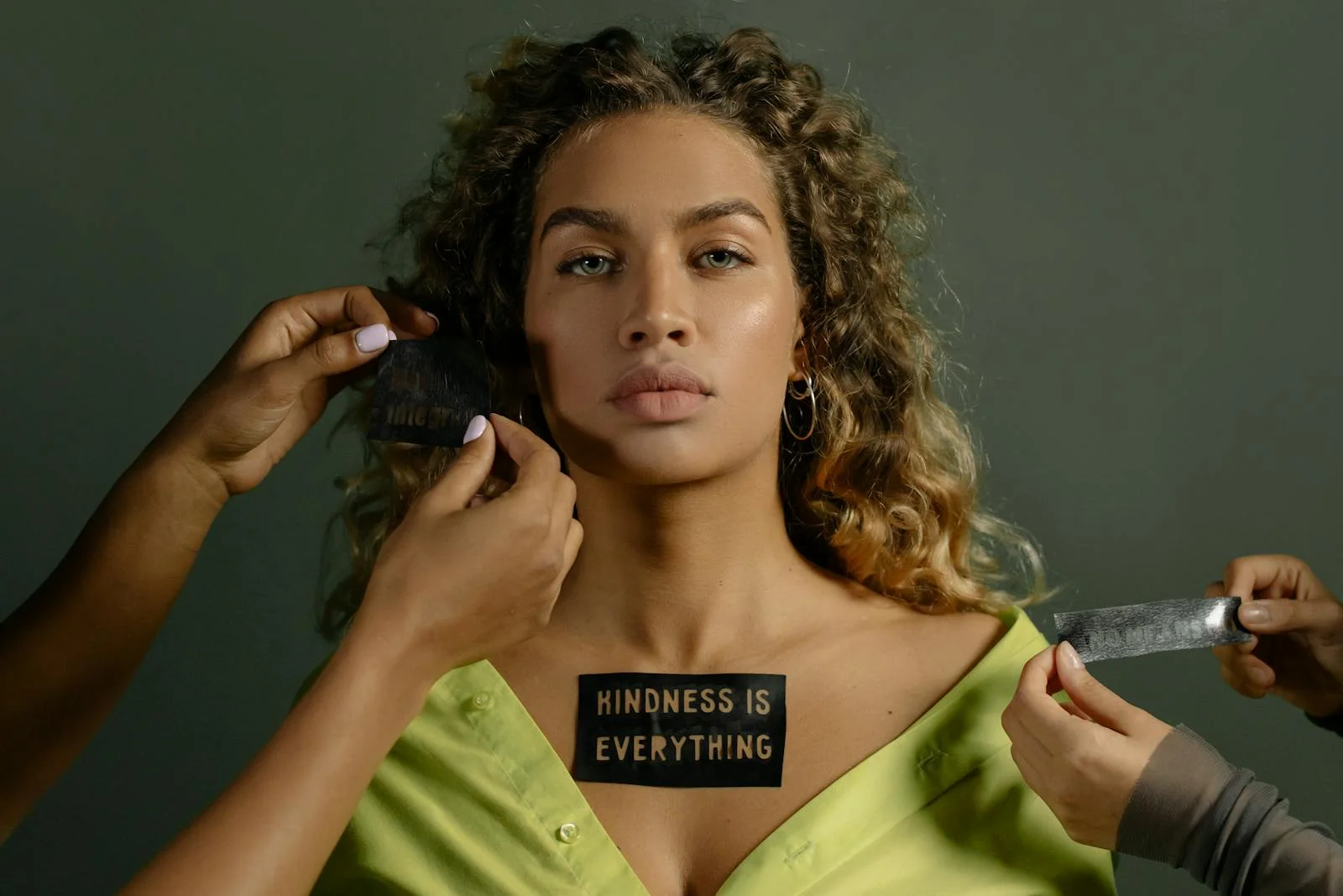A woman with curly hair displays a 'Kindness is Everything' sticker in a powerful portrait.