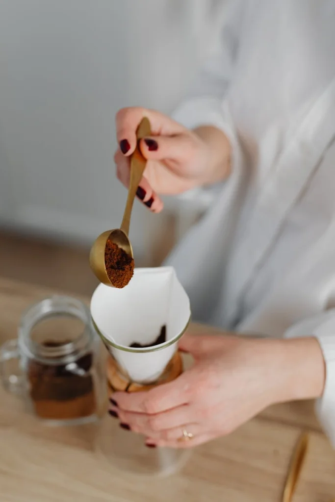 A woman's hands preparing coffee with a Chemex filter on a wooden surface.