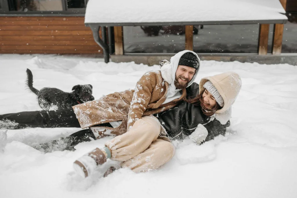 Joyful couple and their dog enjoy playful moments in a snowy landscape.