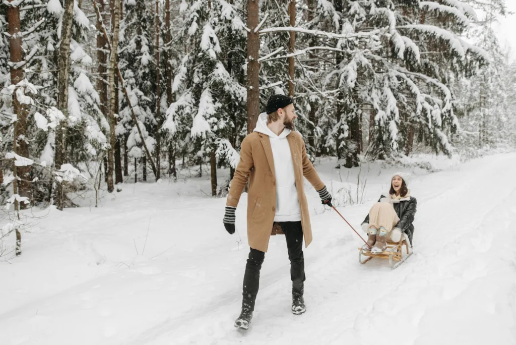 A joyful couple having fun sledding in a snow-covered forest, capturing a playful winter moment.