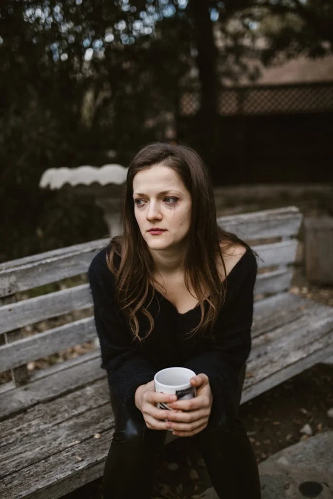 A woman sitting on a bench holding a mug, lost in thought on an autumn day.