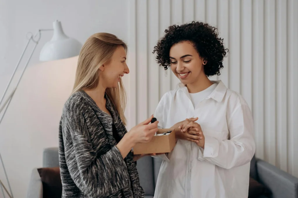 Two women smiling and enjoying essential oils in a cozy indoor setting.