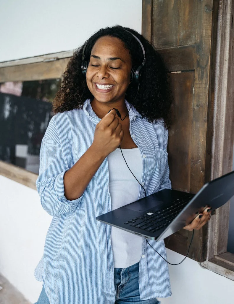 Happy woman listening to music with headphones while using a laptop indoors.