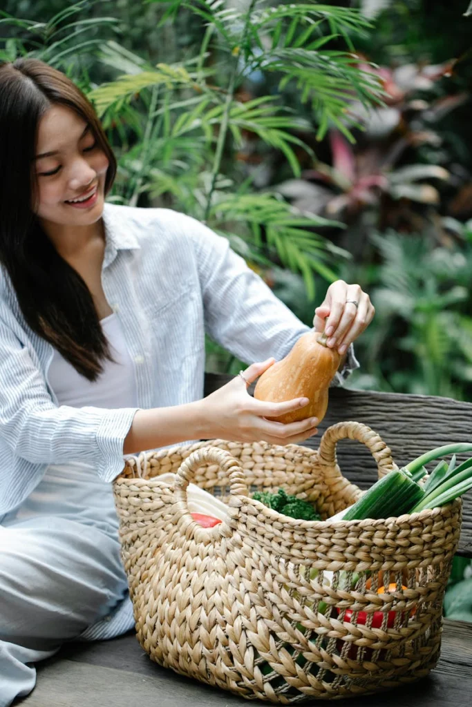 Young woman sitting on bench with basket of fresh vegetables, outdoors.