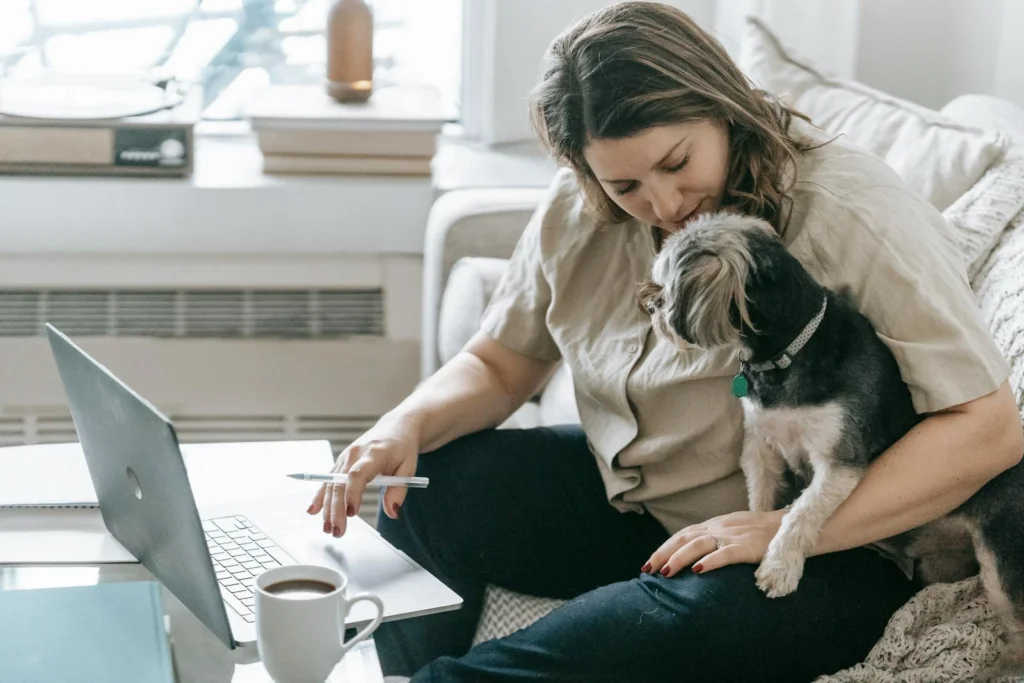 A woman works on her laptop at home with her dog, creating a cozy workspace.