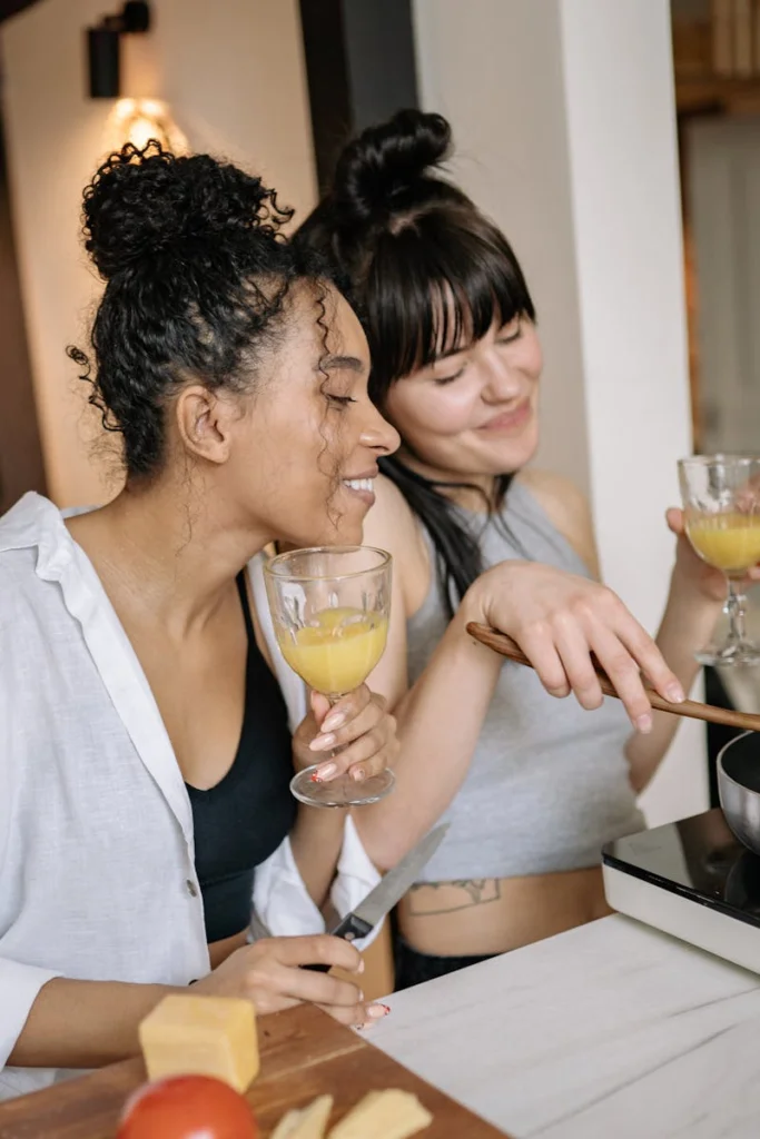 Two women enjoying cooking and drinking juice in a kitchen setting, having fun.