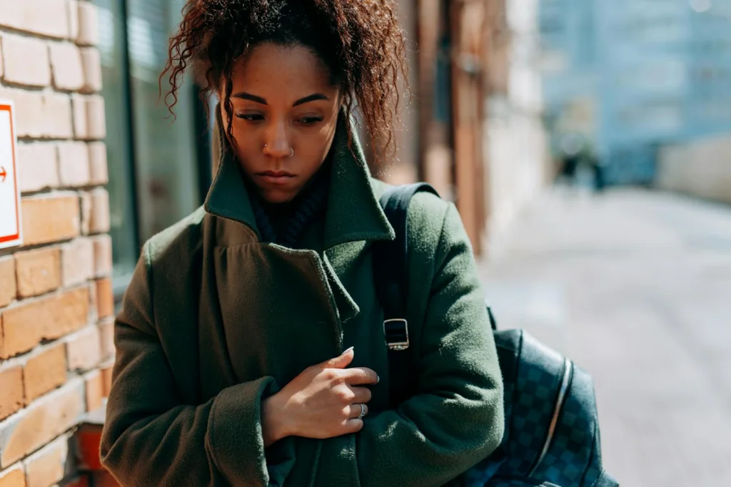 Thoughtful woman in a coat walking down a city street in daylight.