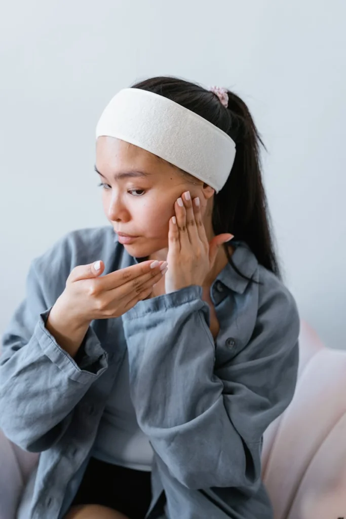 Young woman applying skincare product indoors, promoting healthy skin routine.