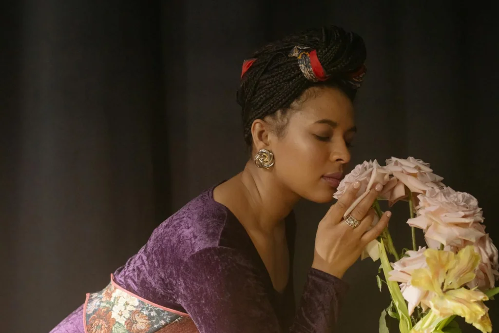 A woman in a velvet dress posing with closed eyes, holding pink roses in a studio setting.