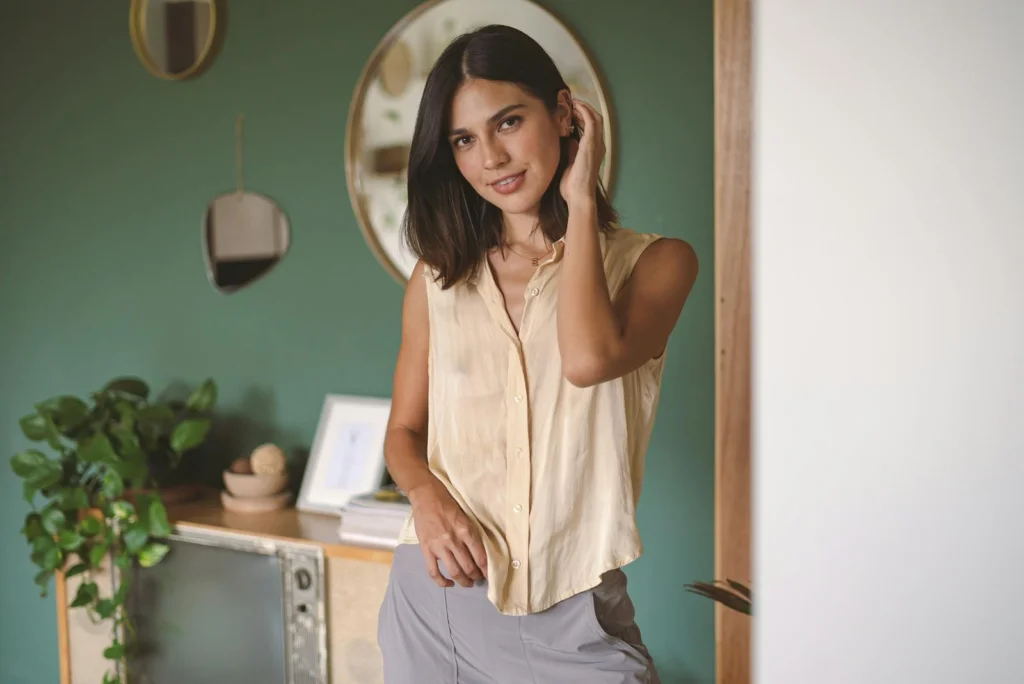 A woman in a casual sleeveless top smiling in a modern, cozy room with green walls.