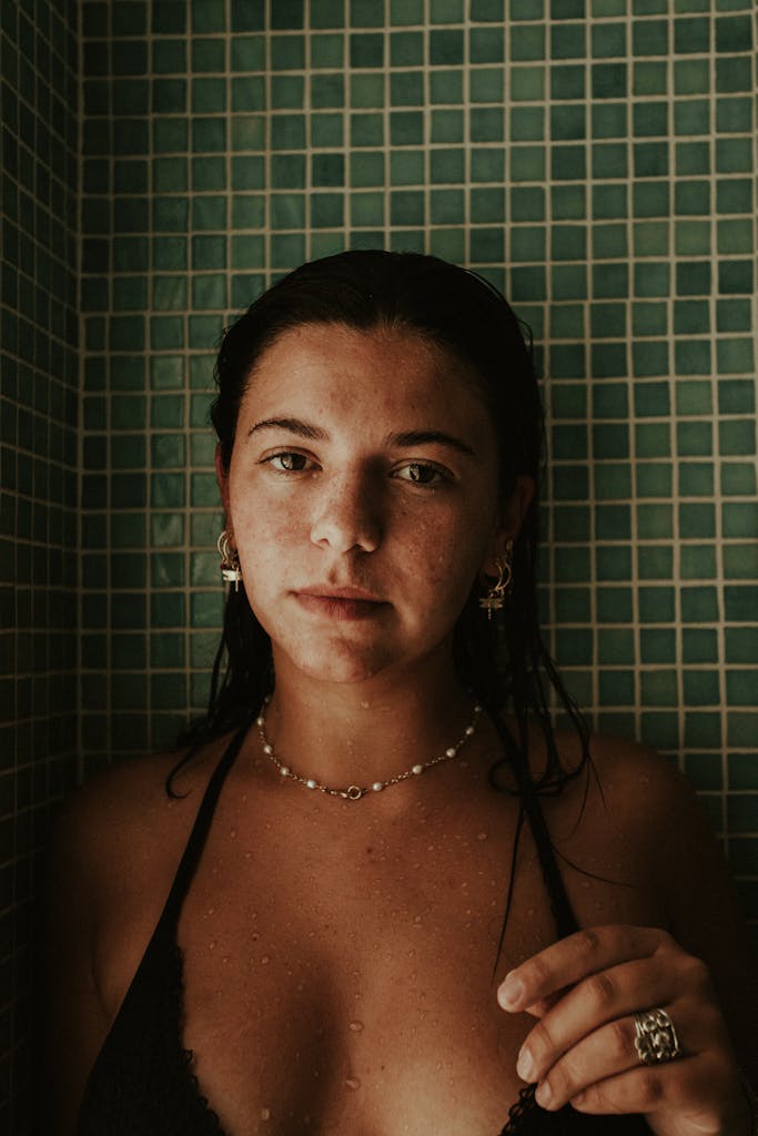 Intimate portrait of a woman standing in a mosaic tiled shower, conveying a moody atmosphere.