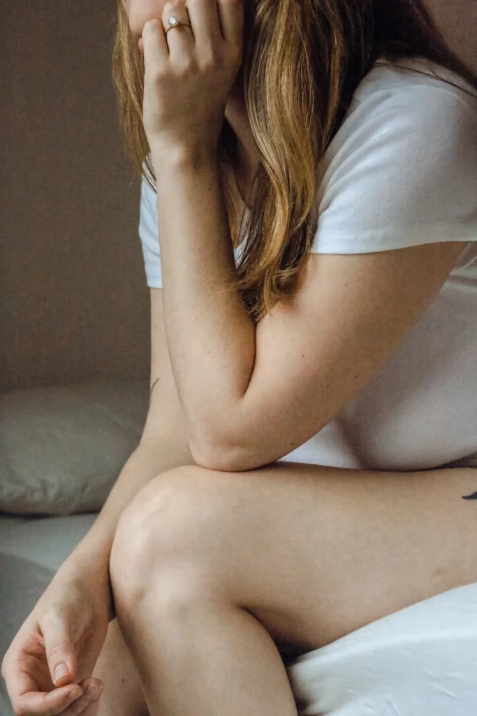 a woman sitting on a bed with her hand on her face