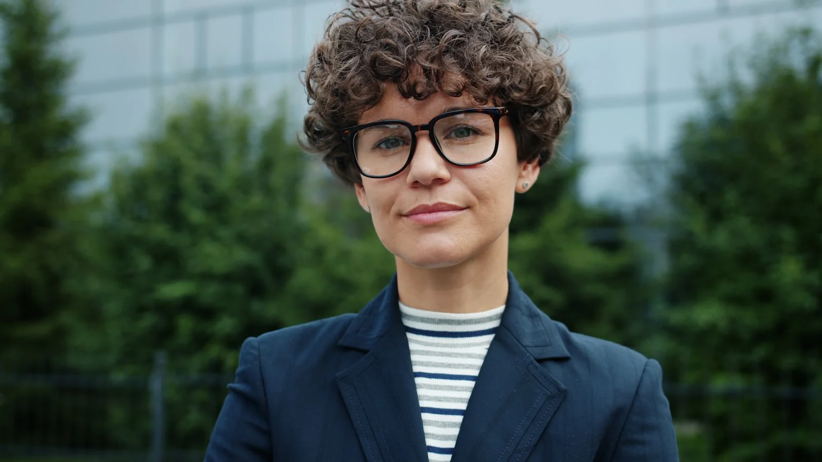 Woman with curly hair and glasses wearing a suit