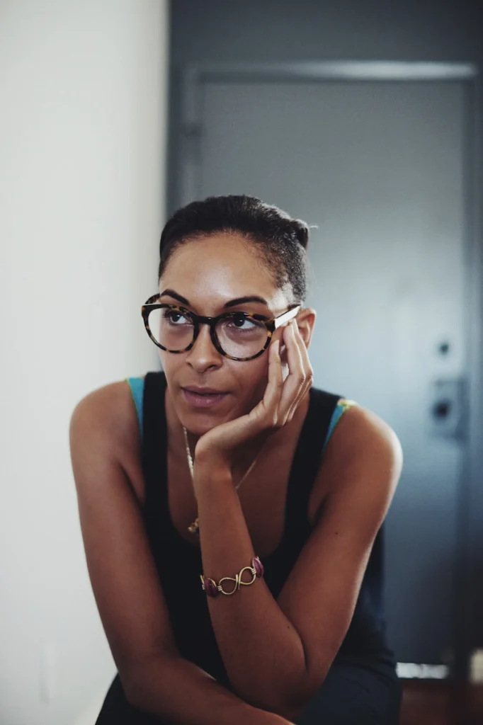 Thoughtful woman wearing glasses sits and ponders.