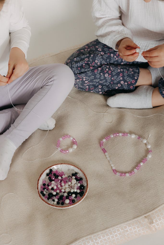 Two children creating beaded jewelry together indoors, showcasing creativity and bonding.