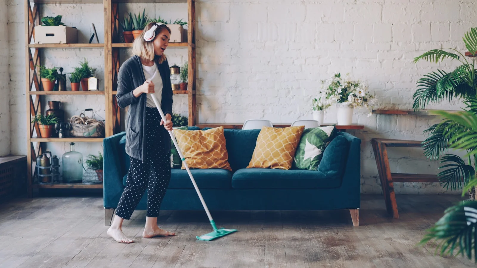 Woman with headphones mops floor in living room