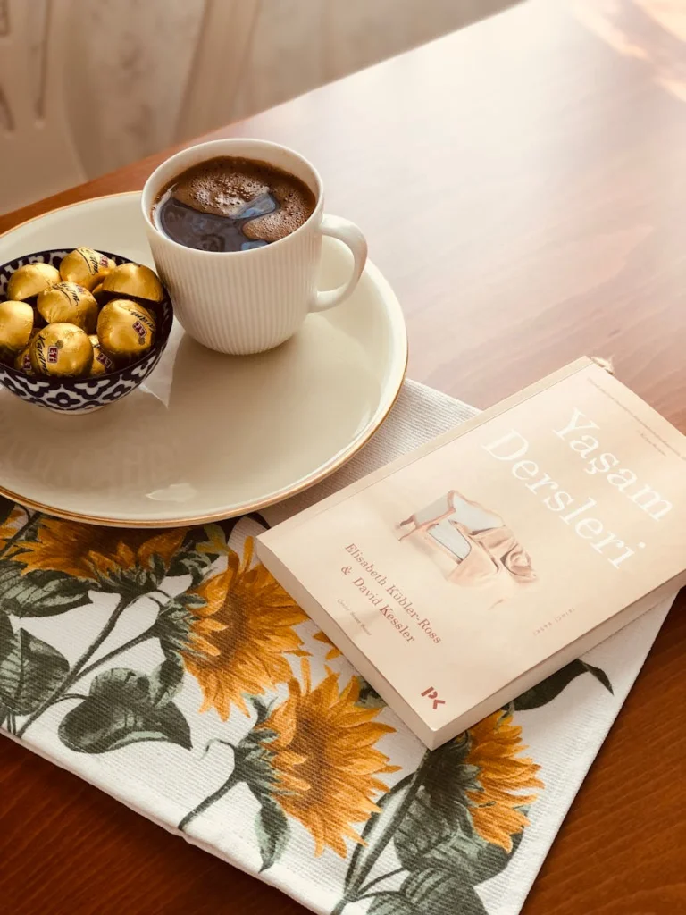 A serene setup with coffee and chocolate beside a book on a printed cloth.