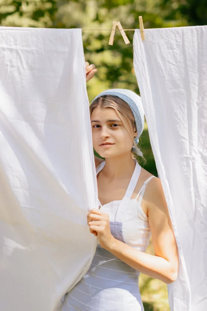 Young woman in apron hanging laundry outdoors, enjoying sunny summer weather.