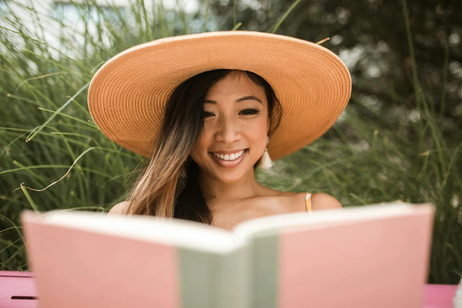 Smiling woman in sun hat reading a book outside in a sunny park.