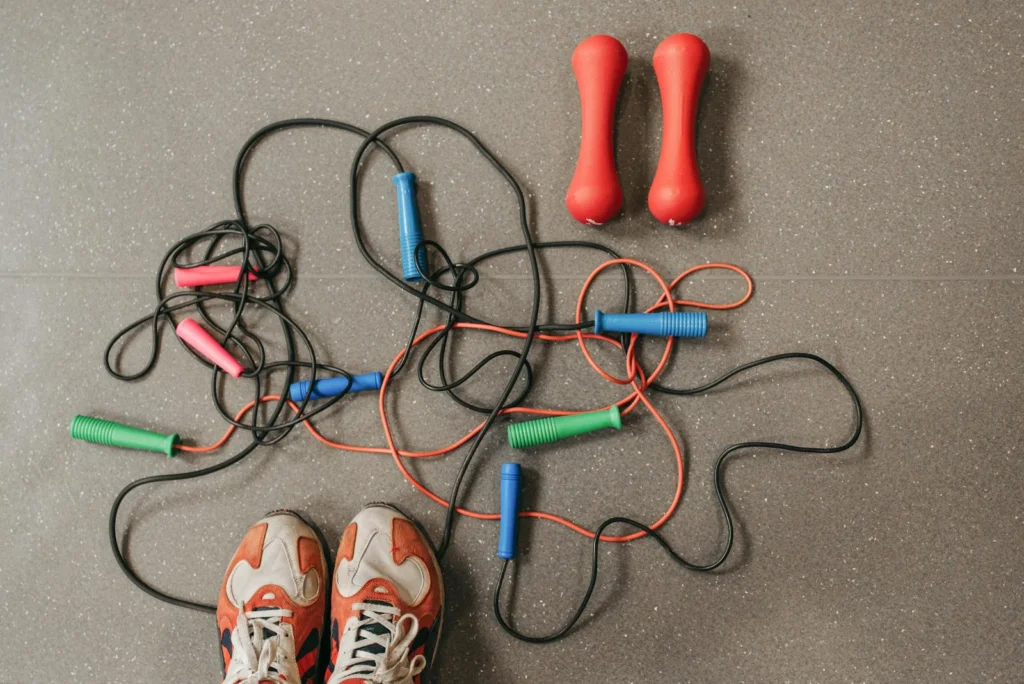 Top view of vibrant jump ropes and dumbbells on a gym floor, with sneakers visible.